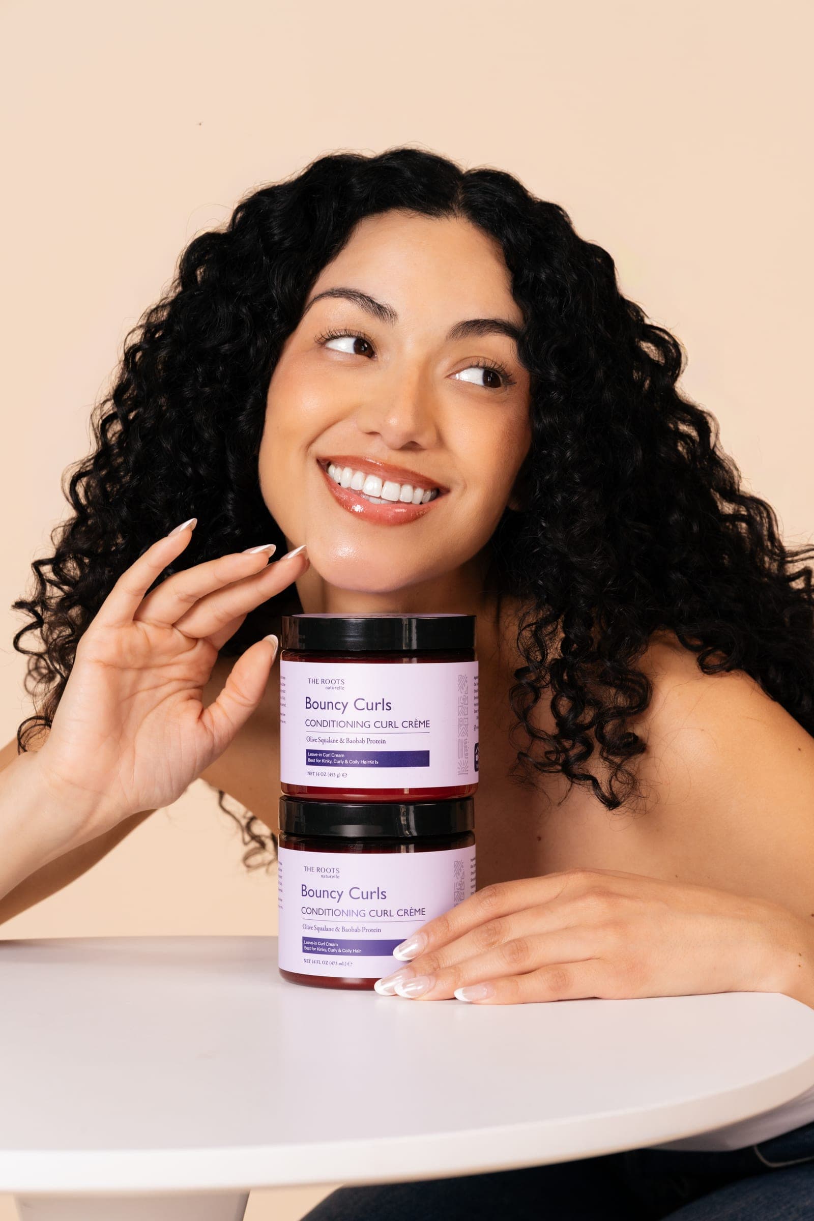 Model with soft, defined curls holding the Bouncy Curls Conditioning Curl Crème
