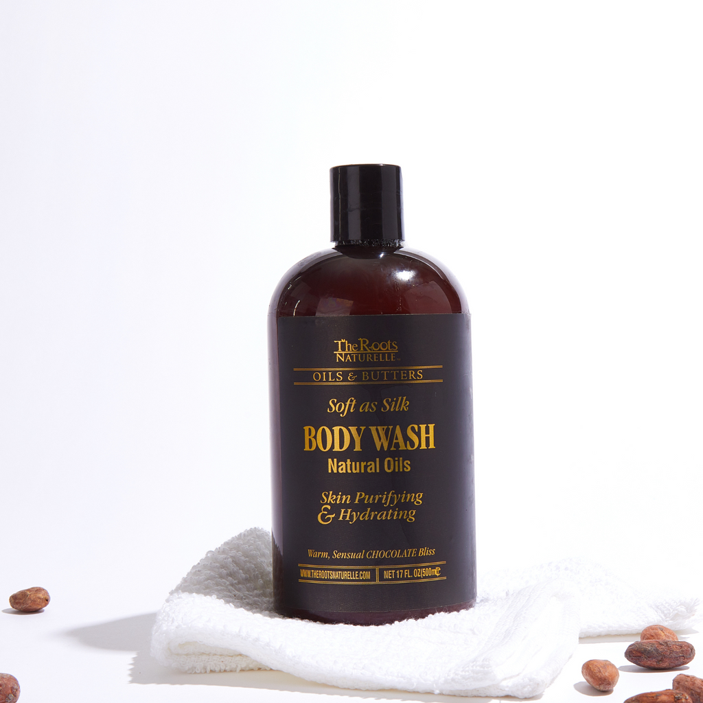 A bottle of Chocolate Bliss Body Wash with a dark label, resting on a white surface with a towel and some cocoa beans scattered around.